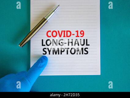 COVID-19 simbolo dei sintomi del codice a lunga distanza. Carta bianca con parole Covid-19 sintomi a lunga distanza. Mano del medico, penna, sfondo blu, spazio di copia. Medico, C. Foto Stock