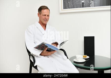 Un uomo d'affari di 50 anni di età di successo che riposa dopo un duro lavoro nella camera privacy di un centro benessere spa, rilassante mentre legge la rivista bef Foto Stock