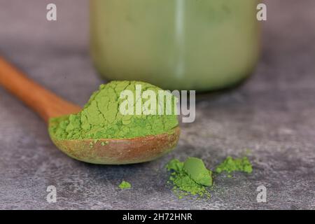 Un primo piano di una paletta di polvere di tè verde matcha con un latte matcha dietro Foto Stock