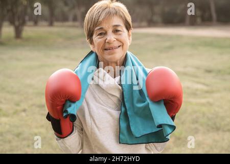 Donna anziana sorridente sulla macchina fotografica dopo l'allenamento di boxe all'aperto al parco cittadino - Focus on Face Foto Stock