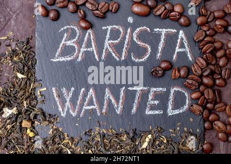 Il barista voleva scrivere con gesso su una piastrella di pietra nera, circondata da chicchi di caffè e foglie verdi di tè Jasmin Foto Stock