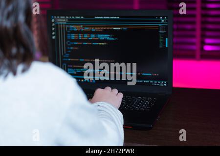 Teenage sviluppatore web programmazione di una pagina web su un laptop nella sua stanza illuminata da luci LED viola. Foto Stock