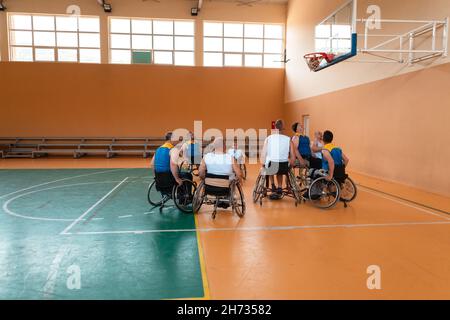 I veterani della guerra disabili hanno mescolato le squadre di pallacanestro di età e di corsa in carrozzina che giocano un match di addestramento in una sala della palestra di sport. Disabili Foto Stock