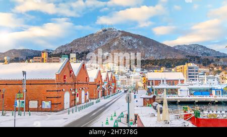 Paesaggio urbano degli storici magazzini in mattoni rossi e del Monte Hakodate al crepuscolo a Hakodate, Hokkaido Giappone in inverno Foto Stock