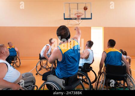 I veterani della guerra disabili hanno mescolato le squadre di pallacanestro di età e di corsa in carrozzina che giocano un match di addestramento in una sala della palestra di sport. Disabili Foto Stock