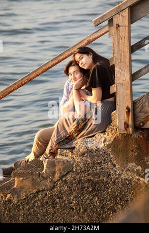Giovane coppia biraciale seduta su gradini di legno che conducono all'acqua Foto Stock