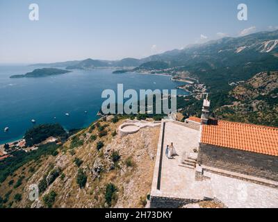 La sposa e lo sposo camminano tenendo le mani abbracciando la piattaforma di osservazione vicino all'antico monastero Foto Stock