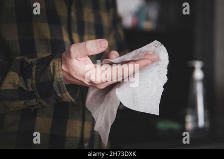 maschio pulisce la mano con un fazzoletto su sfondo scuro. Disinfezione delle mani durante la pandemia del coronavirus. Pulizia delle mani di batteri e germi. Foto Stock