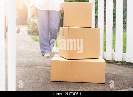 Una donna va alla scatola del pacco consegnata al cancello della casa Foto Stock