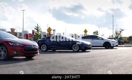 Una Tesla Model S rossa e blu e una Model X bianca vengono visualizzate durante il giorno parcheggiate presso una stazione Supercharger Tesla. Foto Stock