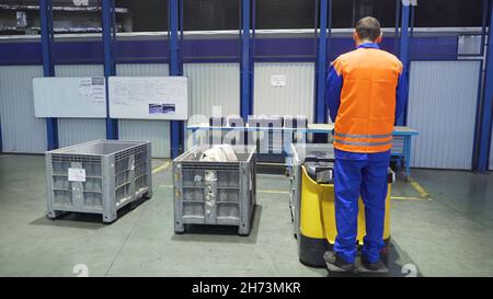 Il lavoratore sul caricatore trasporta le scatole in magazzino. Scena. L'operatore che si trova sul caricatore lo controlla per il trasporto di scatole di carico nel magazzino di fabbrica. Foto Stock