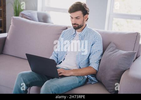 Foto di positivo bearded messo freelancer messo a fuoco uomo sit divano digitando pc e-mail indossare casual vestito in casa confortevole al chiuso Foto Stock