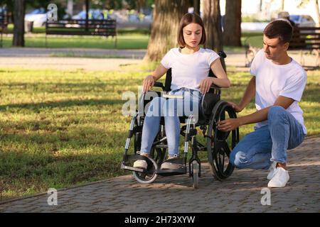 Giovane donna con disabilità fisica e suo marito che ha problemi con la sedia a rotelle nel parco Foto Stock
