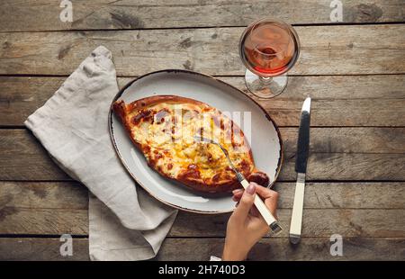 Donna che mangia gustoso khachapuri Ajarian su sfondo tavola di legno Foto Stock