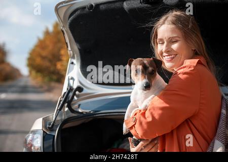 Bella donna con carino Jack Russel terrier vicino auto il giorno d'autunno Foto Stock