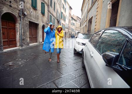 Una giovane coppia innamorata si sta godendo una passeggiata in città in impermeabili in un'atmosfera allegra durante una giornata piovosa. Passeggiata, pioggia, città, rapporto Foto Stock