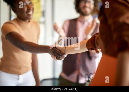 I giovani colleghi si stringono le mani in un'atmosfera amichevole in ufficio Foto Stock