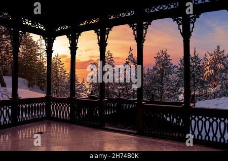 Vista del tramonto sulla foresta di neve ghiacciata con alberi di abete di neve coperti dal balcone in legno. Galleria di legno aperto o gazebo. Foto Stock