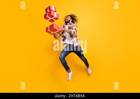 Vista a tutta lunghezza del corpo del ragazzo bello allegro che salta goccia caduta giftbox isolato su sfondo giallo luminoso Foto Stock