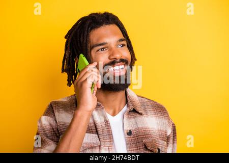 Foto di attraente pelle scura uomo vestito camicia a quadri comunicante moderno dispositivo cercando vuoto spazio isolato colore giallo sfondo Foto Stock