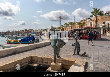 Scultura in bronzo di un pescatore di ritorno dalla pesca sulla banchina del porto villaggio di Marsaxlokk, Marsaxlokk Malta, Europa Foto Stock