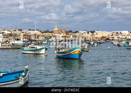 Vista pittoresca del porto di Marsaxlokk con una tradizionale barca da pesca Luzzu più molte altre barche da pesca, villaggio di Marsaxlokk, Malta Foto Stock