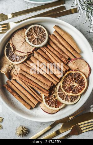 Spezie invernali, mele secche e arance in ciotola bianca su tavolo da cucina grigio con posate dorate. Bastoncini di cannella e frutta invernale per VIN brulé Foto Stock