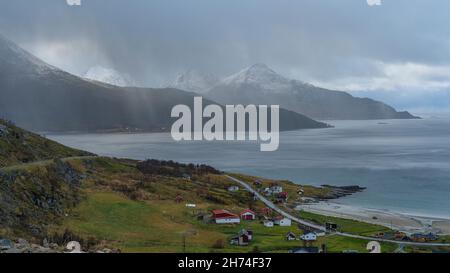 Bucht von Grøtfjord mit der Insel Vengsøya im Hintergrund. Herbst in Troms, Norwegen, gelbe Wiesen, verschneite Berge und bunte Häuser. Facciata posteriore Foto Stock