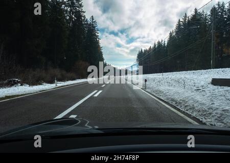 Un colpo in movimento da dietro il parabrezza di un'auto elettrica con montagne innevate delle alpi. Freddo nuvoloso giorno d'autunno. Foto vista POV in prima persona Foto Stock