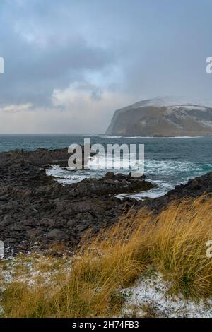 Sturmfront bei Kamøyvær auf Magerøya, Norwegen, mit der Insel Gáhpesuolu. Wilde Küste mit rot weissem Leuchtturm, gelbem Gras und brechenden Wellen. Foto Stock