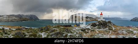 Sturmfront bei Kamøyvær auf Magerøya, Norwegen, mit der Insel Gáhpesuolu. Wilde Küste mit rot weissem Leuchtturm, gelbem Gras und brechenden Wellen. Foto Stock