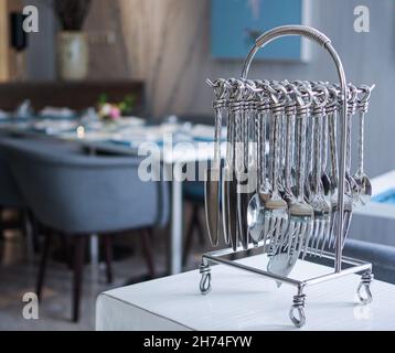 Elegante coltelleria in acciaio inossidabile color argento, posate, cucchiai, forchette, coltelli, appendiabiti, rack su tavolo da ristorante bianco Foto Stock