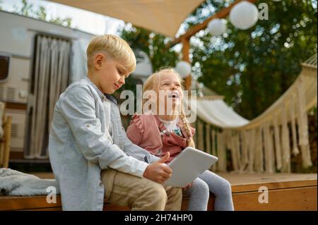 Sorridendo i bambini che usano il computer portatile al rimorchio, in campeggio Foto Stock