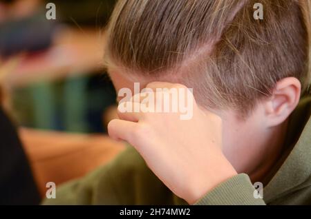 un ragazzo che sta pensando, concentrandosi su una prova, con la mano che gli sostiene la fronte Foto Stock