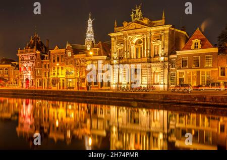 Haarlem, Paesi Bassi, 19 novembre 2021: Facciate storiche si riflettono nelle acque del fiume Spaarne di notte, con sullo sfondo la torre di Sain Foto Stock