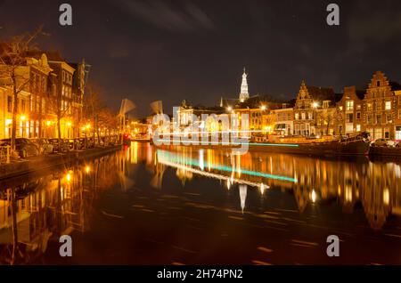 Haarlem, Paesi Bassi, 19 novembre 2021: Vista lungo il fiume Spaarne di notte con un percorso leggero di una barca che ha appena superato un ponte levatoio aperto Foto Stock