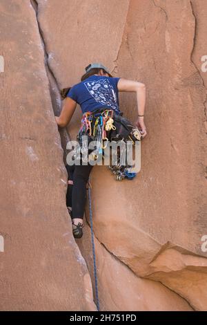 Un arrampicatore di piombo che seleziona una camma dalla sua cremagliera di ingranaggio per disporre in una spaccatura su una salita su Wall Street vicino Moab, Utah. Foto Stock