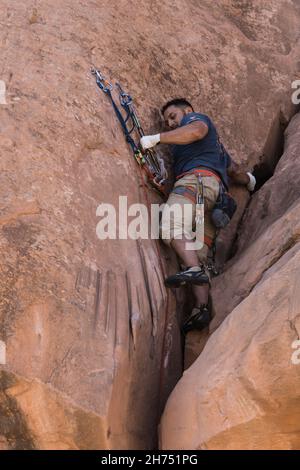 Un arrampicatore riorganizza l'hardware sugli ancoraggi su un percorso nell'area di arrampicata di Wall Street, Moab, Utah. Foto Stock