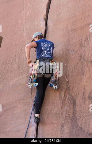 Un arrampicatore di piombo che seleziona una camma dalla sua cremagliera di ingranaggio per disporre in una spaccatura su una salita su Wall Street vicino Moab, Utah. Foto Stock