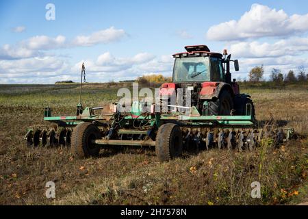 Aratura di un trattore pesante durante la coltivazione di lavori agricoli in un campo con aratro Foto Stock