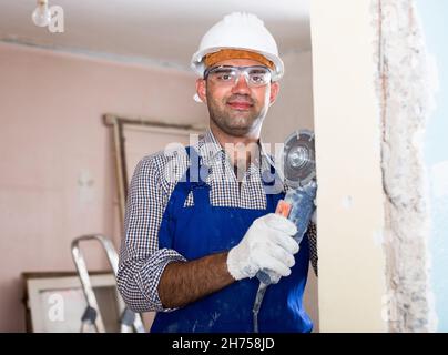 L'ingegnere in casco sta segando la parete con sega circolare Foto Stock