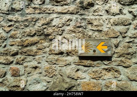 Primo piano di Scallop simbolo della strada di Santiago con una freccia su un muro di pietra in Cantabria, Spagna. Foto Stock