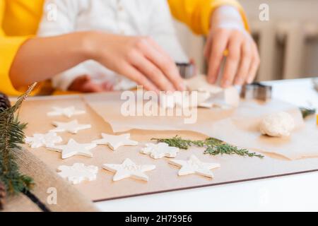 Una donna taglia i biscotti dall'impasto sotto forma di fiocchi di neve. Dolci di Natale fatti in casa. Primo piano con le mani. Foto Stock