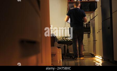 Vista posteriore di un uomo che cammina verso un cassetto aperto contro il banco di ricevimento. Interno di un piccolo ostello con reception e un frigorifero, alloggio economico Foto Stock