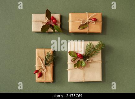 Quattro regali di Natale avvolti in carta riciclata ecologica con fianchi di rose, bacche di wintergreen e rami di abete rosso Foto Stock