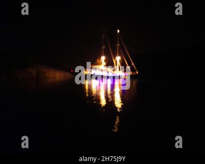 Vista notturna di una grande barca illuminata sopra l'orizzonte. Le luci multicolore che emanano dallo yacht si riflettono sulla superficie del mare. SH Foto Stock