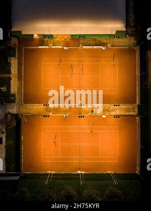 Vista dall'alto, vista aerea di alcune persone che giocano a tennis su un campo di argilla di notte. Foto Stock