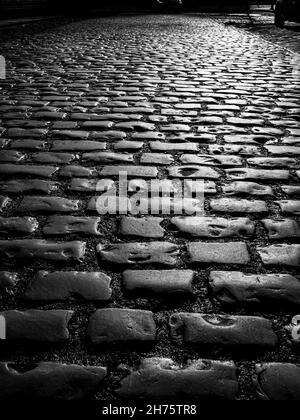 vista ravvicinata che si affaccia su vecchi ciottoli sulla strada in bianco e nero Foto Stock