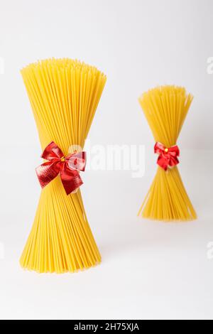 Un mazzo verticale, un mazzo di spaghetti crudi legati con una corda con un arco rosso. Fascio su sfondo bianco. Il concetto di cucina italiana per le vacanze. Foto Stock