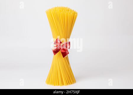 Un mazzo verticale, un mazzo di spaghetti crudi legati con una corda con un arco rosso. Fascio su sfondo bianco. Il concetto di cucina italiana per le vacanze. Foto Stock